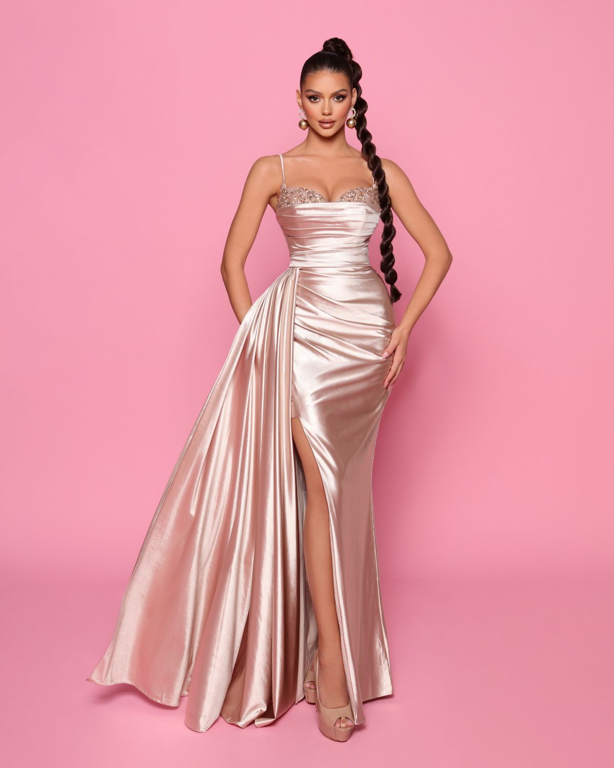 Woman wearing a pink satin evening gown with a high slit on a pink background