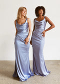Two women wearing long, light blue satin dresses against a plain background.