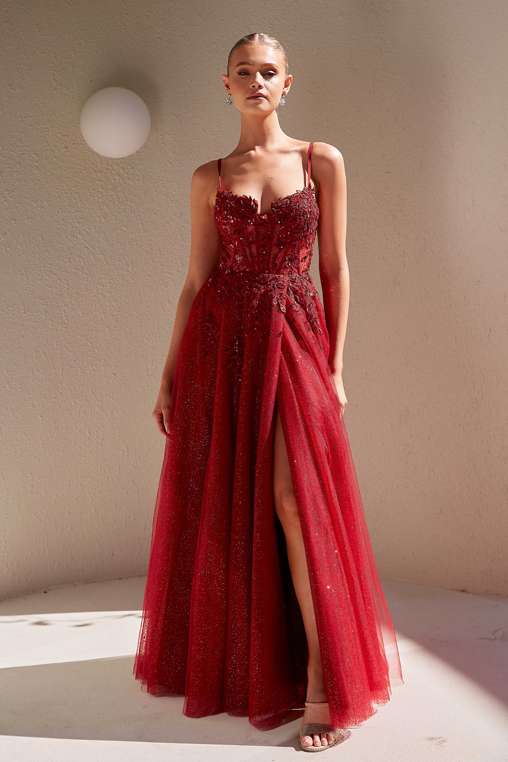 Woman wearing a red evening gown with a slit in a softly lit room.