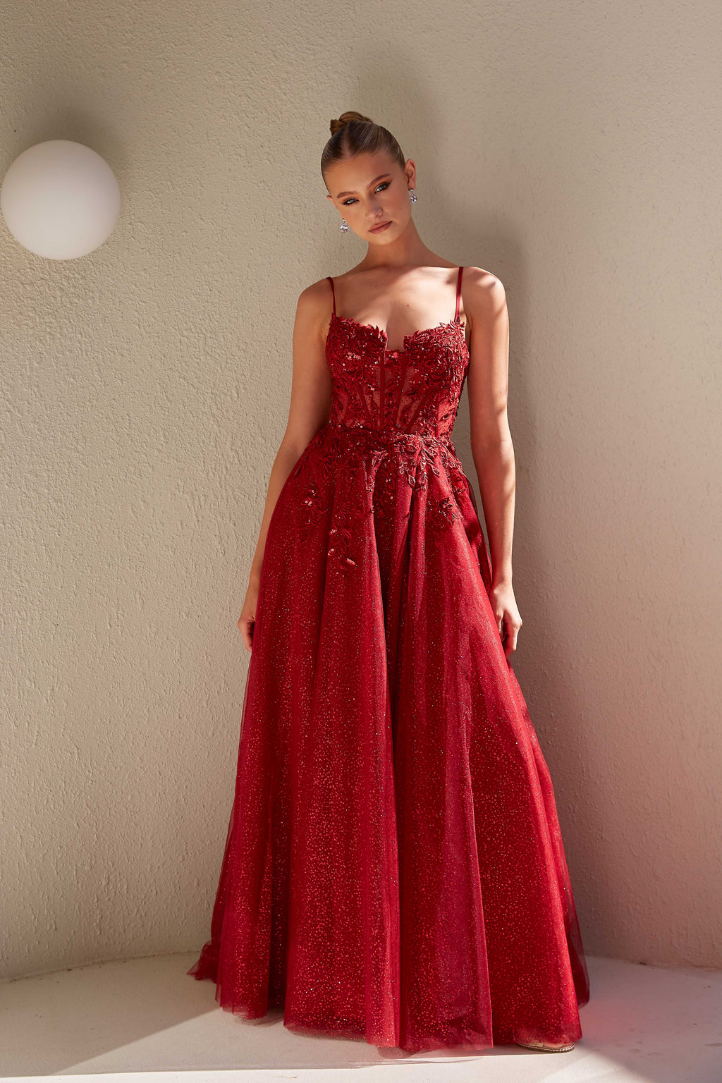 Woman wearing a red lace dress against a plain wall.