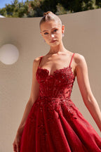 Woman wearing a red evening gown with intricate detailing against a beige wall.