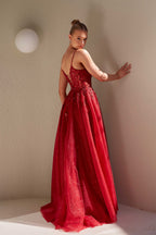 Woman in a red evening gown standing against a plain wall.