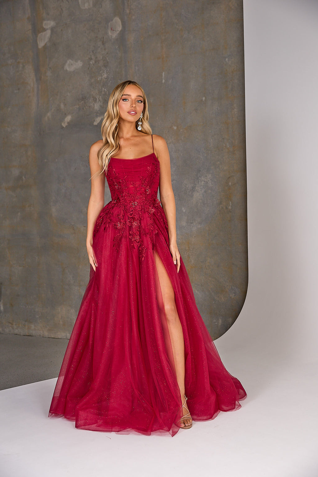 Woman wearing a red evening gown with a slit on a neutral background