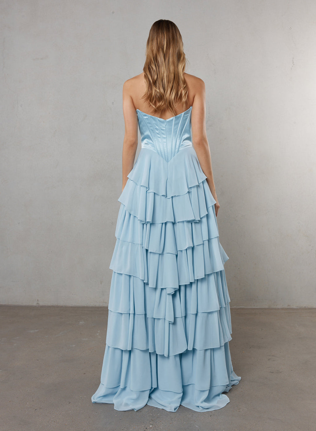 Woman wearing a light blue, tiered dress against a plain background