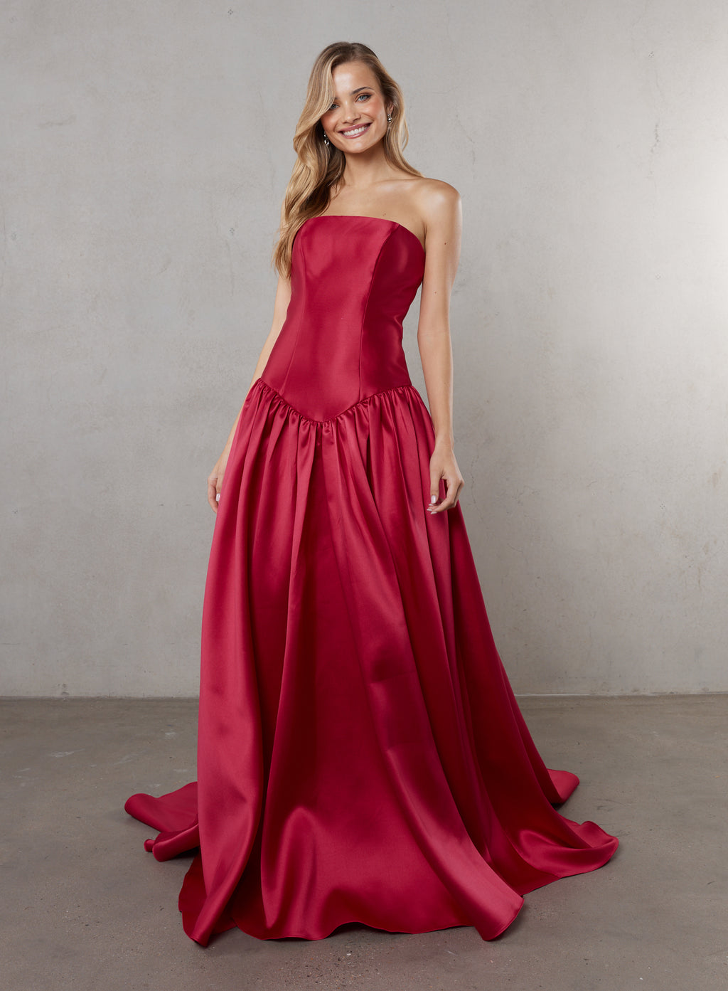 Woman wearing a strapless red gown against a plain background