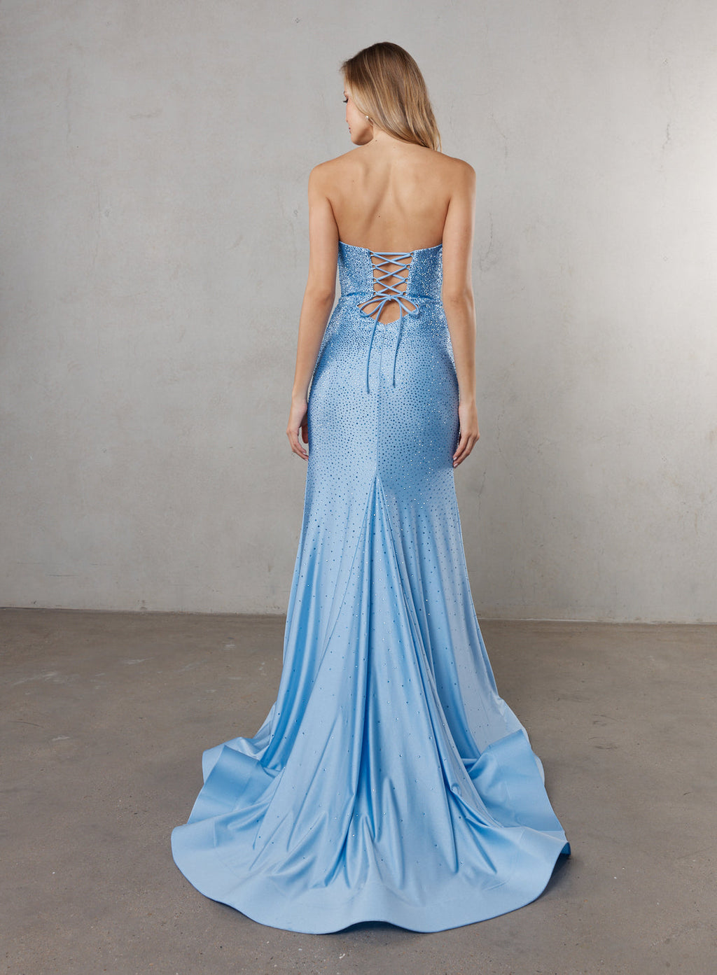 Woman wearing a blue strapless gown with a lace-up back against a plain background