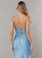 Woman wearing a blue strapless dress with lace-up back against a gray background