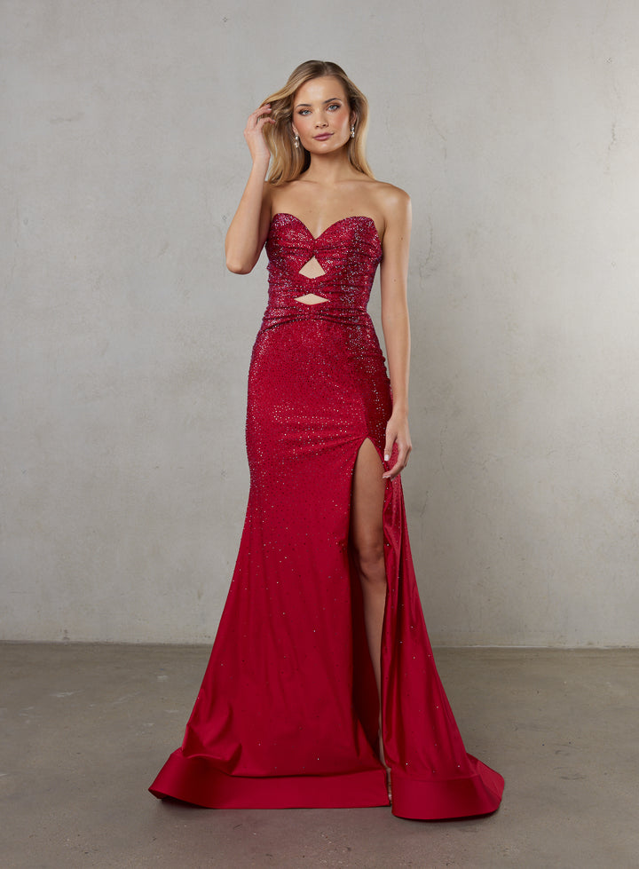 Woman wearing a red strapless evening gown with cut-out details and a high slit on a plain background