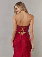 Woman wearing a red strapless dress with lace-up back on a plain background