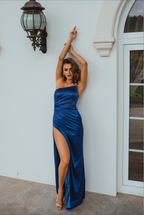 Woman in a blue evening gown standing against a white wall.