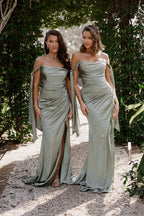 Two women in matching silver dresses standing outdoors with greenery in the background