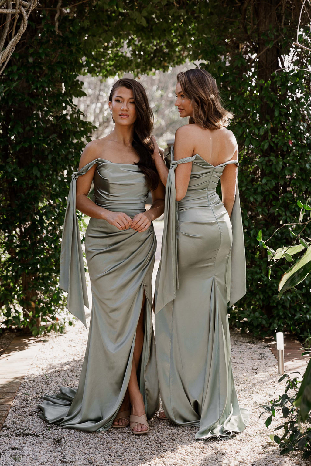 Two women in matching green dresses standing outdoors with greenery in the background