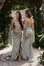 Two women in matching green dresses standing outdoors with greenery in the background