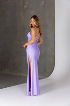 Woman wearing a purple dress with a slit, standing against a neutral background