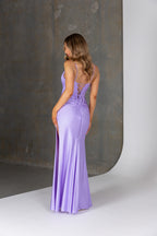 Woman wearing a purple evening gown with a backless design against a neutral background