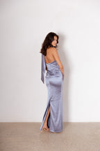 Woman wearing a silver evening gown with a slit, standing against a white wall.