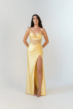 Woman wearing a yellow evening gown with a slit on a white background