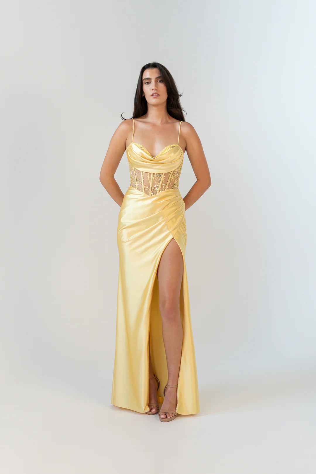 Woman wearing a yellow evening gown with a slit on a white background