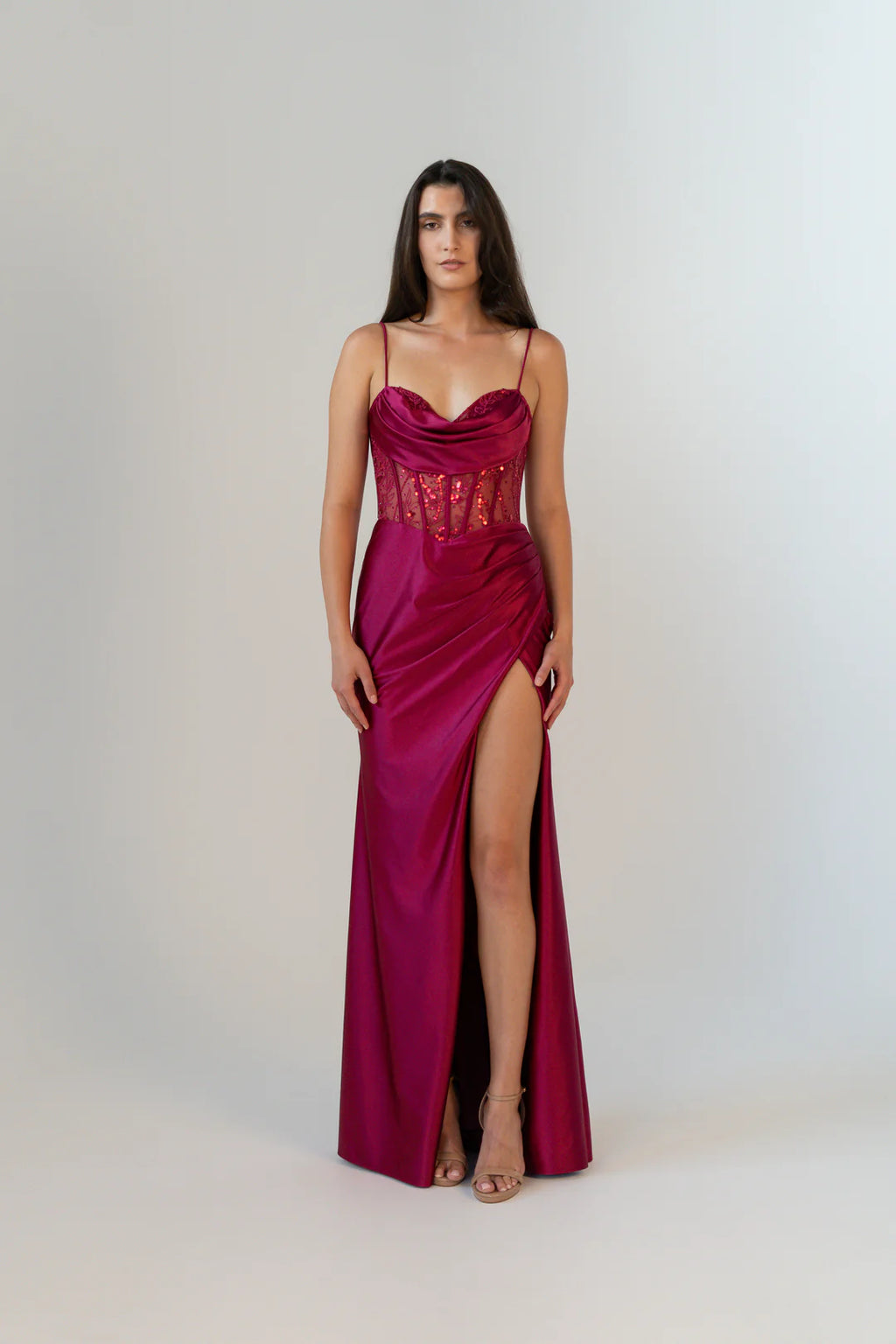 Woman wearing a vibrant red evening gown with a high slit on a white background