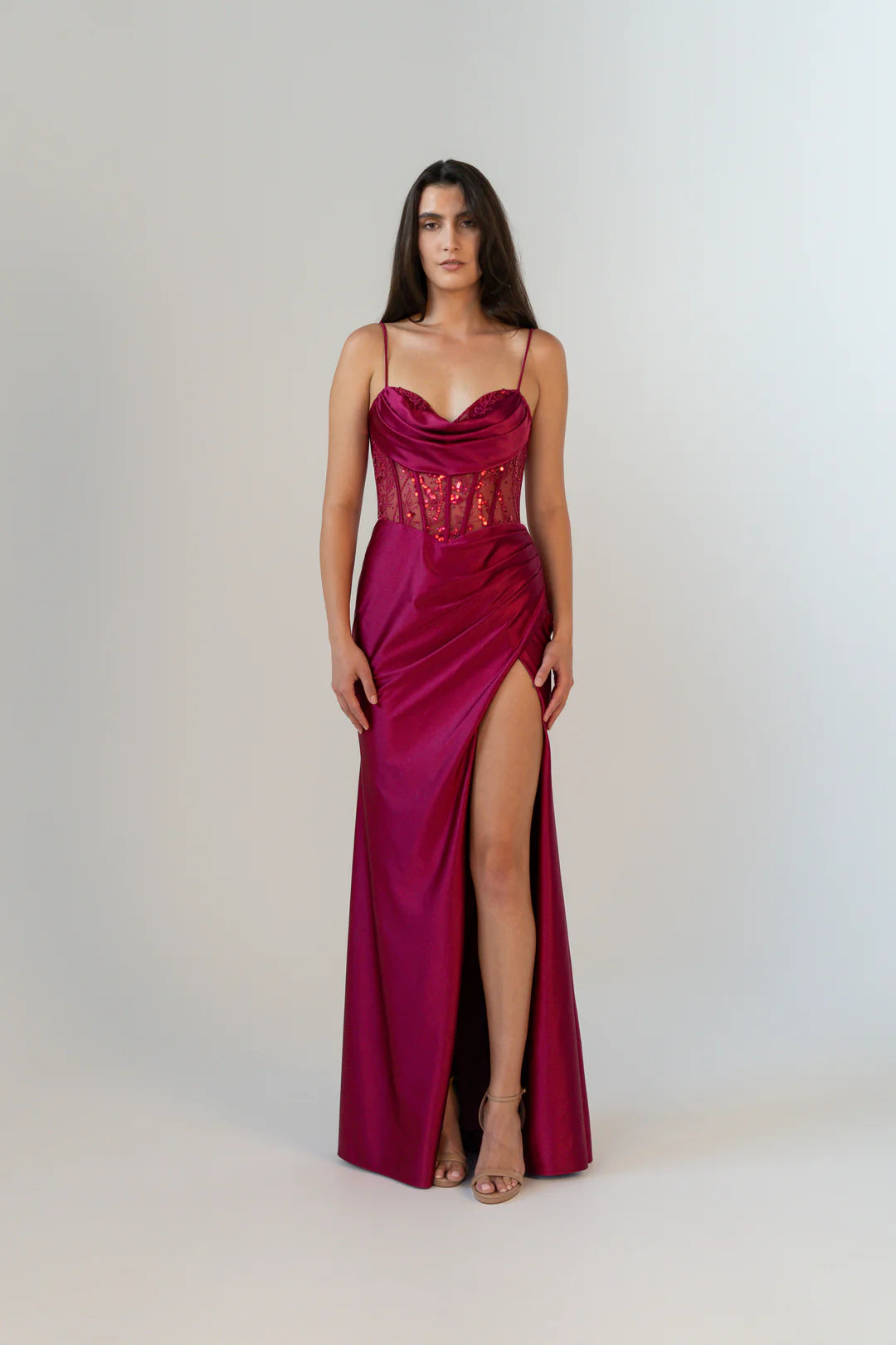 Woman wearing a vibrant red evening gown with a high slit on a white background