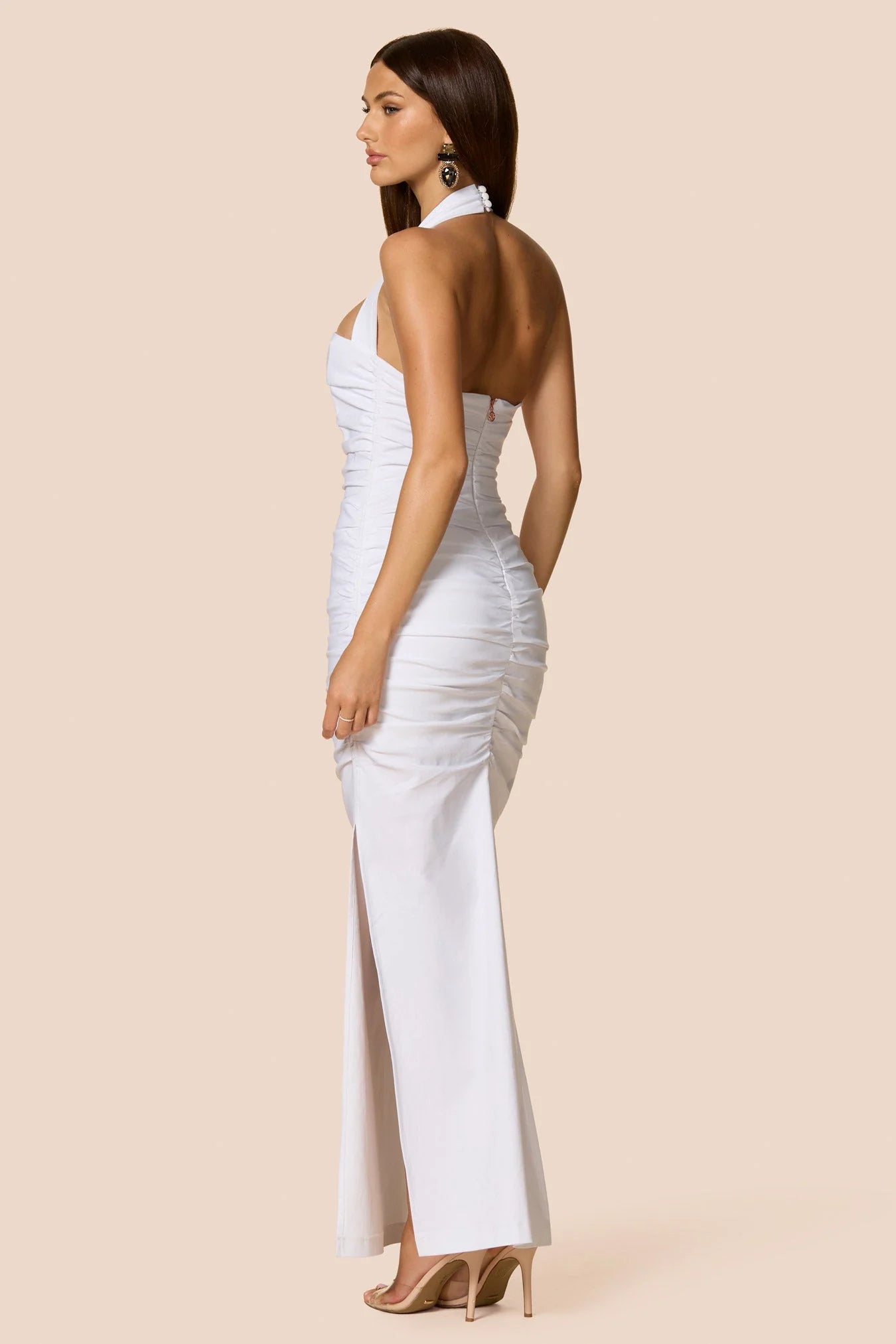 Woman wearing a white strapless dress with a high slit on a beige background